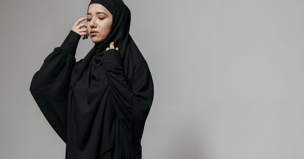 Woman in a navy and cream open abaya raising one arm to show the wide kimono-cut sleeve and its contrast cuff band