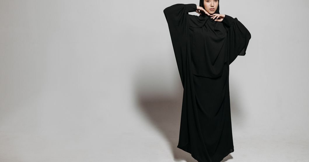 Woman in a flowing brown satin butterfly abaya with wide wing sleeves and a gold embellished front panel