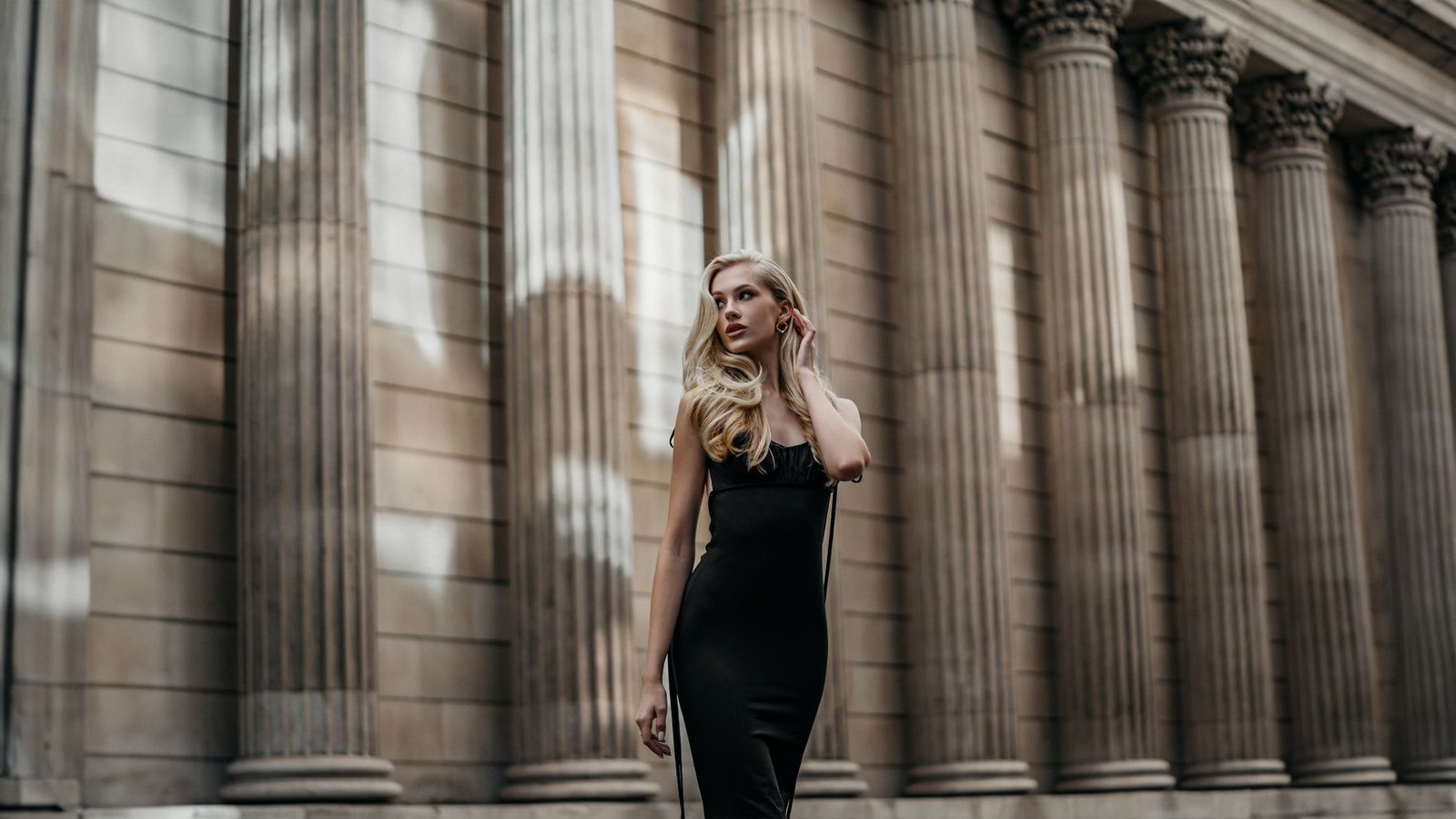 Woman in a sculpted black dress posing against architectural columns
