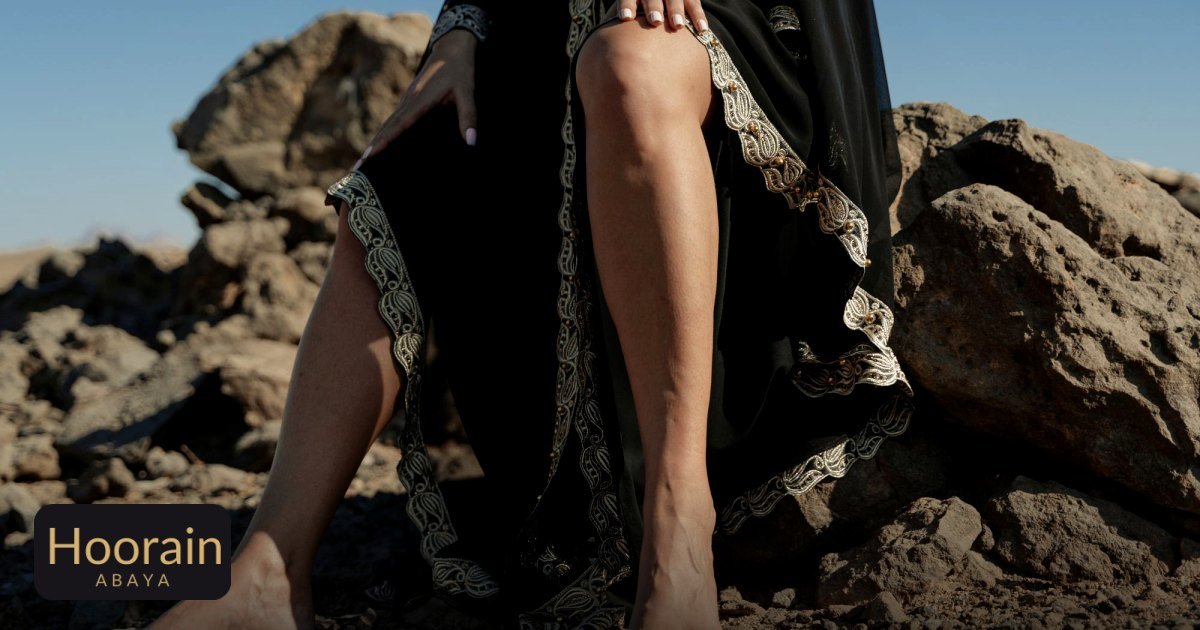 Abaya Fabrics Guide: Crepe, Nida, Chiffon and Linen - a woman sitting on rocks, wearing an abaya, under a clear blue sky